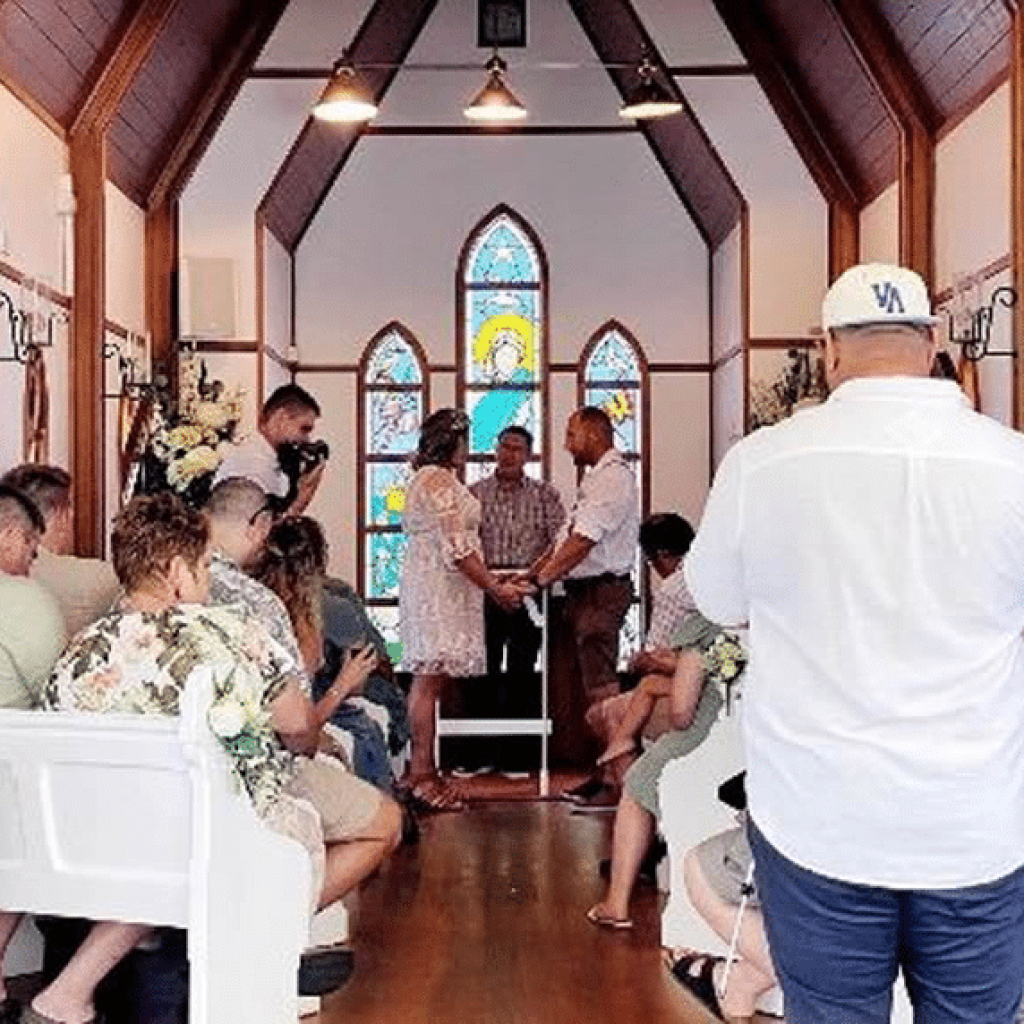 A wedding ceremony inside the floating chapel, with a couple standing before a pastor and stained glass windows in the background.