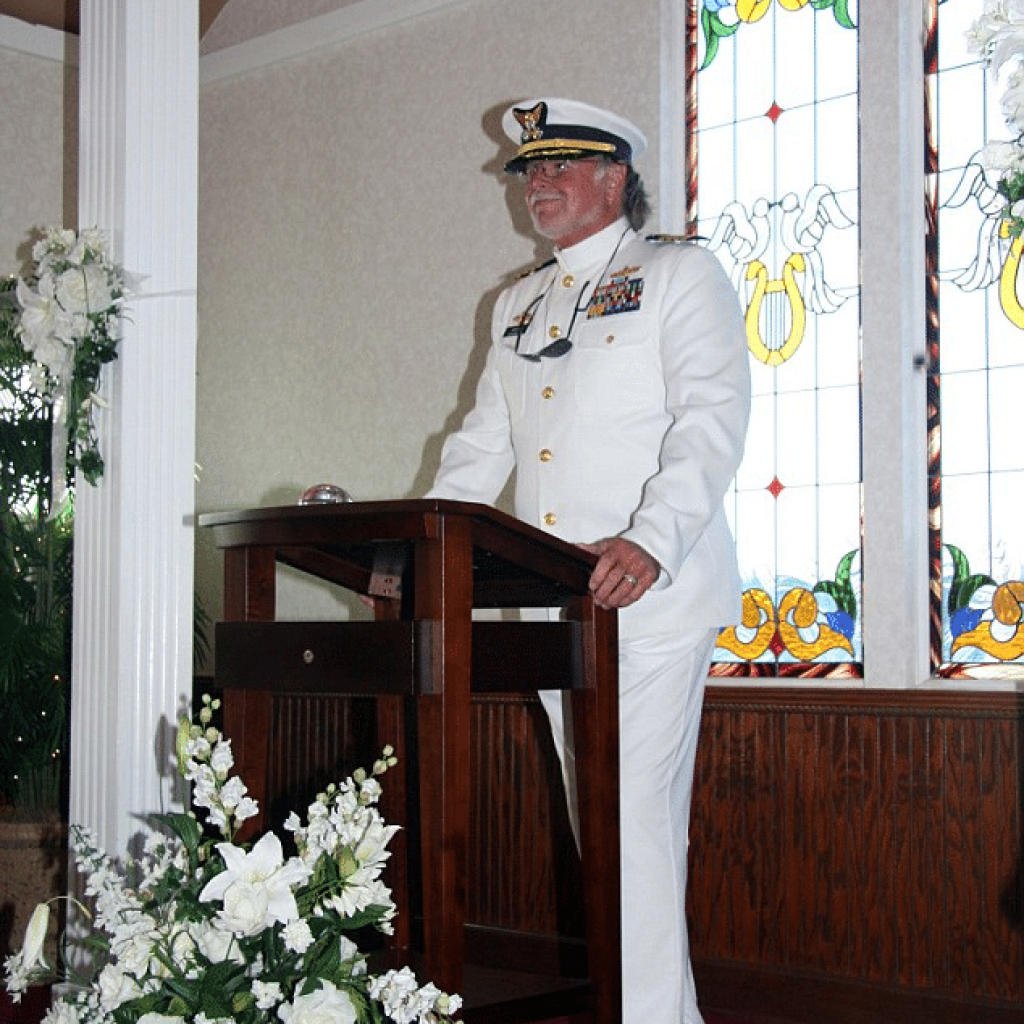 Captain Jerry Orca in a white uniform officiating a wedding inside the floating chapel with stained glass windows in the background.