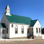 Side angle of a church building with tall, arched windows and a green metal roof.