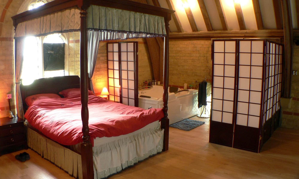 A shot of a serene bedroom with a four-poster bed, wooden beams, and a Shoji screen divider.