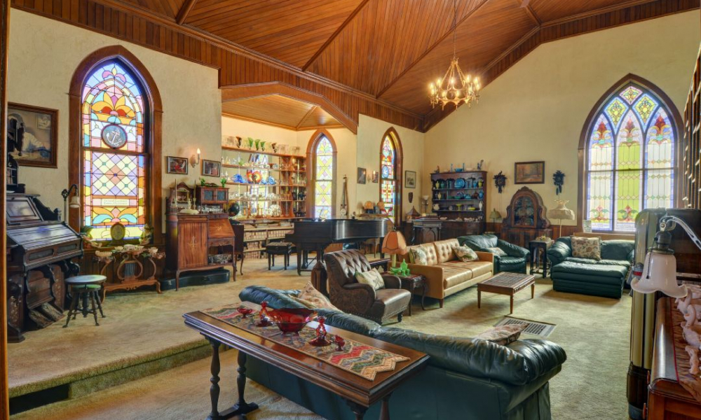 A spacious living room with vaulted wooden ceilings, stained glass windows, and a mix of vintage and modern furnishings.